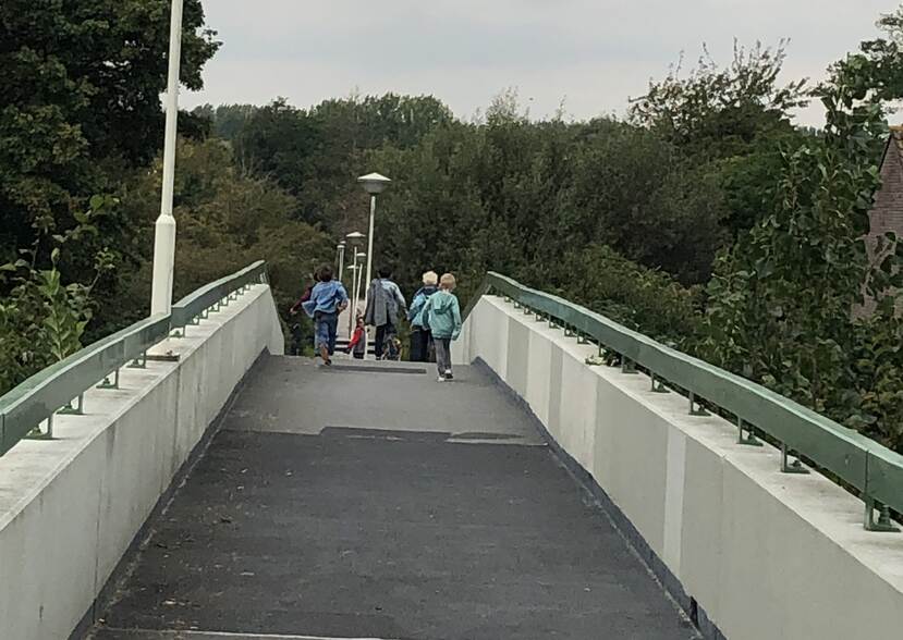 Een brug in de looprichting. Aan andere kant van de brug, aan de overkant: een groepje kinderen op de rug bezien.