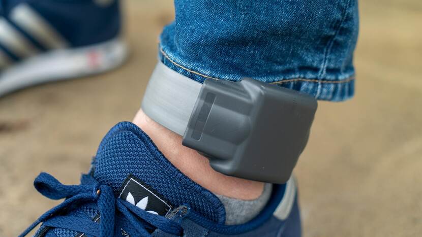 Elektronische enkelband om een enkel met daaronder een voet in een sportschoen.