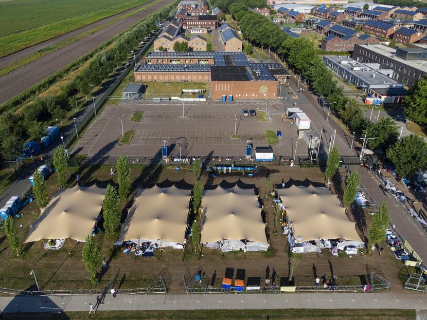 Dronefoto van het aanmeldcentrum in Ter Apel. Op de voorgrond grote zonnetenten, daar achter een sporthal en daar achter de gebouwen van het AZC.