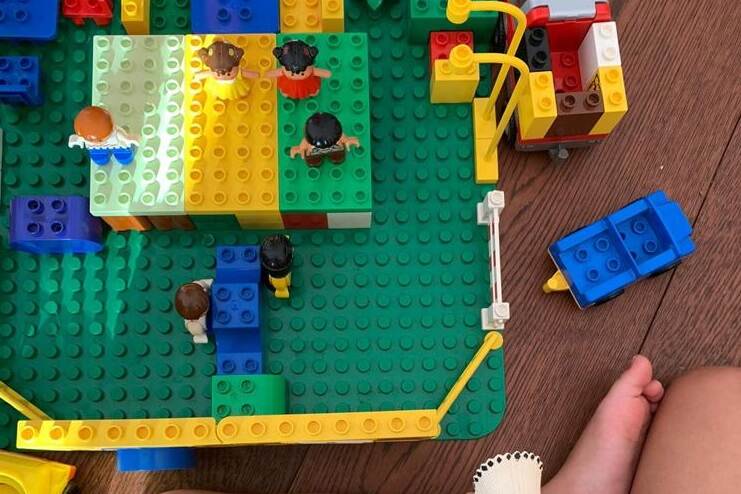 Een huisje van Lego speelgoed met poppetjes van bovenaf gezien, met in onderin beeld een kindervoetje in beeld van het kind wat er mee speelt.