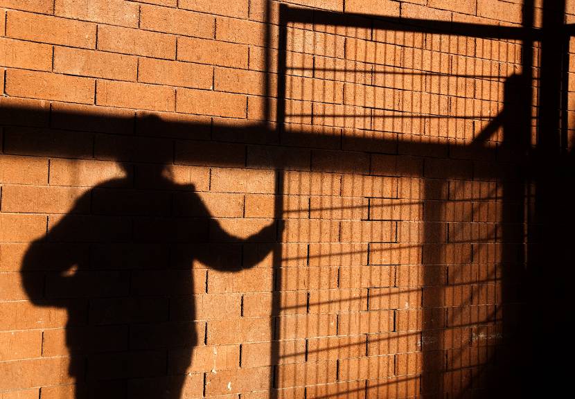 Schaduw van een jongere in een Justitiële Jeugd Instelling. Een hek is te zien.