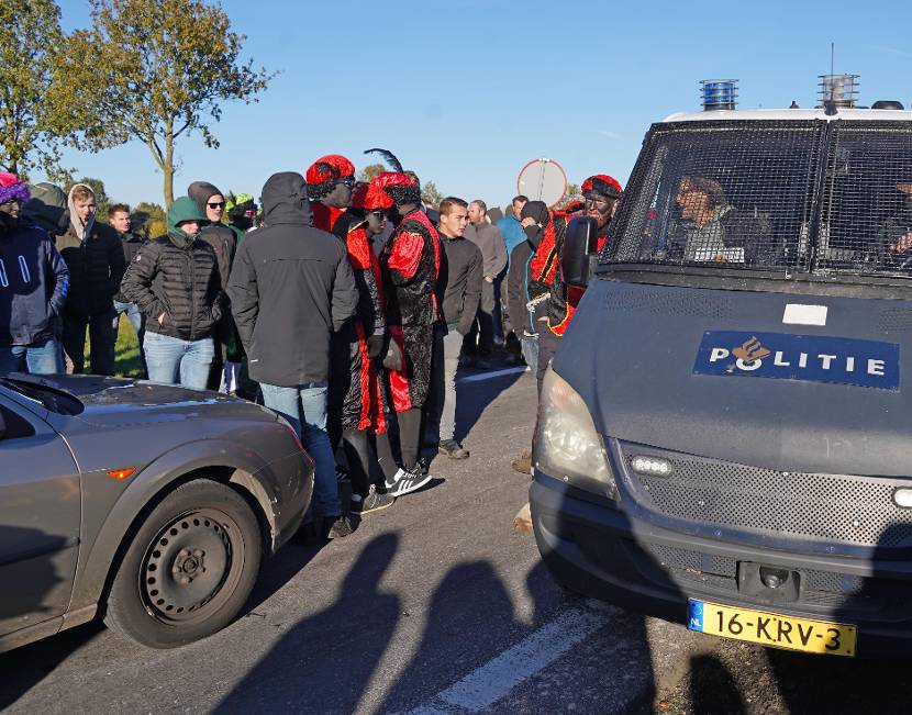 Protesterende mensen, waarvan een aantal in zwartepietenpak met daarnaast een politiebusje.