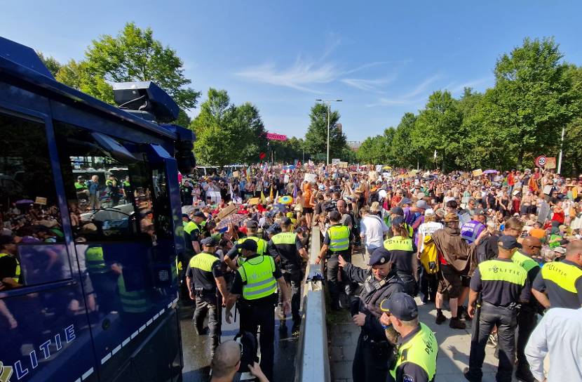 Een demonstratie met veel demonstranten. Op de voorgrond politieagenten en een politiebus.